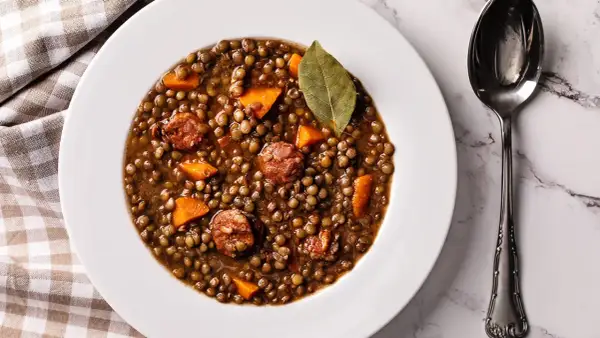 Un plato de lentejas estofadas con trozos de zanahoria y chorizo, decorado con una hoja de laurel.