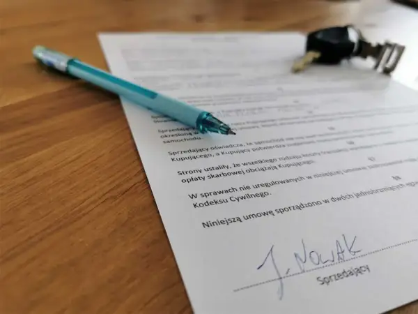 Długopis i kluczyki leżą na dokumencie, który pomoże Ci dowiedzieć się, jak spisać umowę kupna-sprzedaży samochodu.