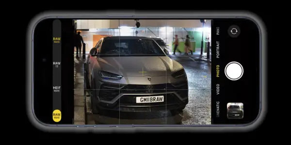 Un'auto sportiva grigia, con targa GMIIBRAW, inquadrata dall'app fotocamera di un iPhone con opzione apple proraw attiva.