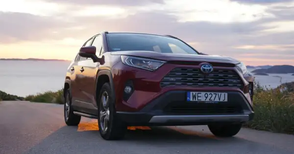Czerwona Toyota RAV4 2.5 Hybrid na tle zachodzącego słońca nad morzem. Niskie spalanie to jej atut.