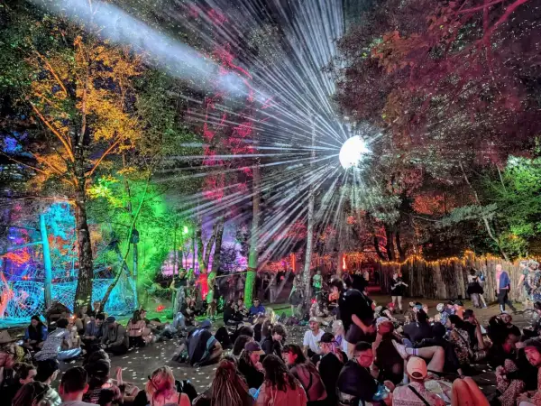 Bunte Lichter und ein Discoball erhellen den Wald, während eine Menge auf dem Boden sitzt. Das ist die Magie des Fusion Festival Lineups!