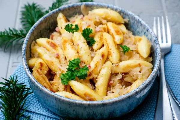 Herzhafte Bubespitzle mit Sauerkraut und Speck, garniert mit Petersilie, in einer blauen Schüssel.