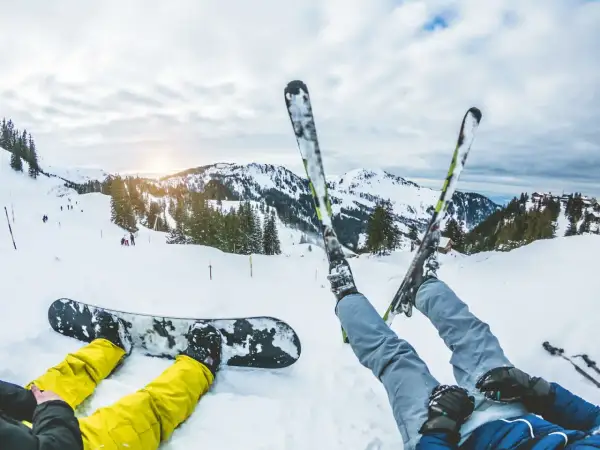 Narciarz i snowboardzista odpoczywają na stoku. Zastanawiasz się, co bardziej obciąża kolana: narty czy snowboard? Góry i słońce zachęcają do jazdy.