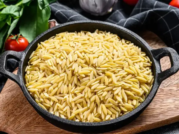 Czarny garnek pełen makaronu w kształcie ryżu, gotowy na pyszne danie.