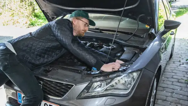 Man med keps och glasögon böjer sig över motorhuven för att byta halogenlampa.