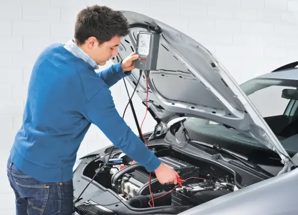 Uomo effettua manutenzione batteria auto con un tester Bosch.