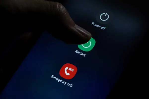 Palec naciska przycisk "Restart" na ekranie telefonu, co może pomóc, gdy zastanawiasz się, jak przywrócić poprzednie ustawienia telefonu.