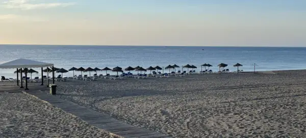 Playa marina de la torre con arena fina y tumbonas bajo sombrillas. El mar tranquilo se extiende hasta el horizonte.