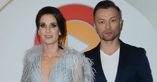 Sylwia Grzeszczak i Liber pozują do zdjęcia. Ona w błyszczącej sukni z piórami, on w granatowej marynarce.