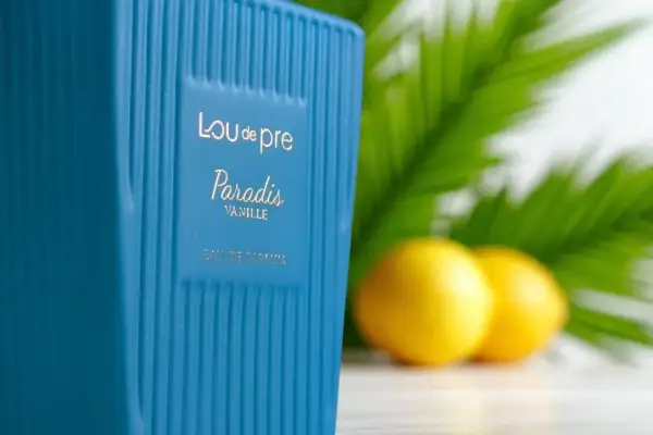 Niebieska butelka perfum Lou de Pre Paradis Vanille na tle liści i cytryn.
