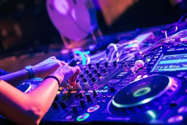 Hände am DJ-Pult, die verschiedene techno subgenres mit Lichtern und Reglern mischen.