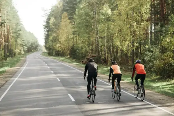 Trzech rowerzystów jedzie obok siebie leśną drogą. Czy można jechać rowerem obok siebie? Tak, jeśli droga jest wystarczająco szeroka i bezpieczna.