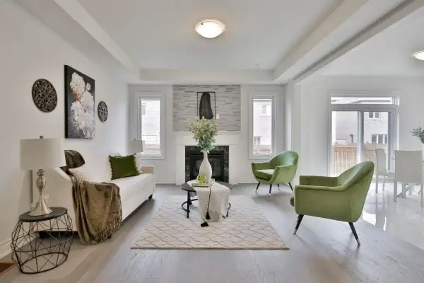 Salon moderne avec canapé blanc, fauteuils verts et cheminée. Le tapis et les coussins apportent une touche de blanc cassé.