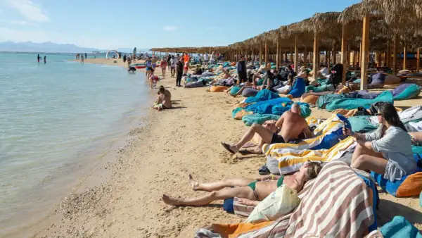 Ludzie odpoczywają na plaży w Egipcie. Idealna pogoda w Egipcie w grudniu sprzyja relaksowi na leżakach pod palmowymi zacienionymi wiatami.