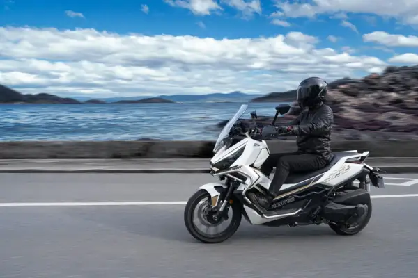Conductor en moto Zontes 368G blanca, con paisaje marino y montañas. ¡Las opiniones sobre esta moto son excelentes!