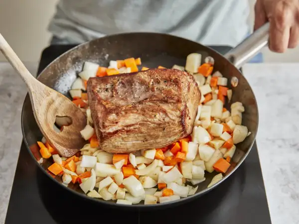 Ein gebratener Rinderbraten ruht auf gewürfeltem Wurzelgemüse in einer Pfanne. Perfekt für ein herzhaftes rinderbraten rezept.