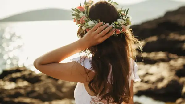 Frau mit Blumenkranz am Kopf, genießt die Sonne am Meer. Ein Bild von Mittsommer Ritualen.