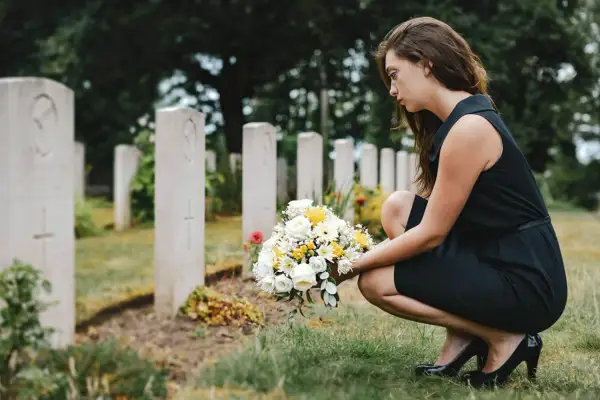 Smutna kobieta w czarnej sukience klęczy przy grobie z bukietem kwiatów. W jej oczach widać ból, jakby szukała pocieszenia w cytatach dla zmarłego dziecka.