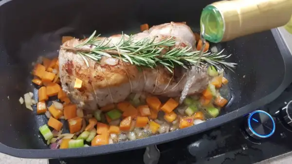 Arrosto di vitello in pentola con verdure e rosmarino, mentre viene sfumato con vino bianco.
