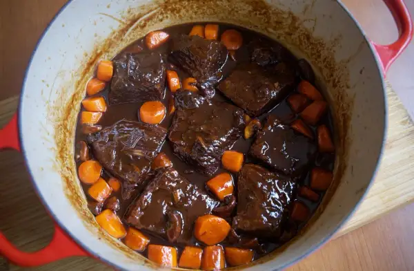 Sabroso plato típico de Francia: ternera estofada en salsa oscura con zanahorias y champiñones en una olla roja.