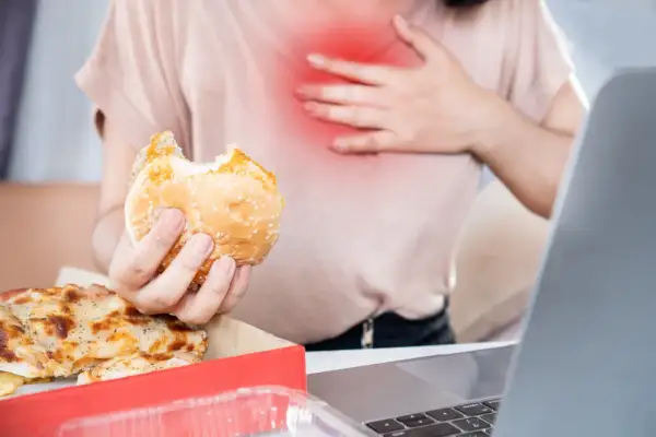 Osoba z bólem w klatce piersiowej trzyma gryzionego burgera. Obok pizza. Zastanawia się, co jeść na zgagę.