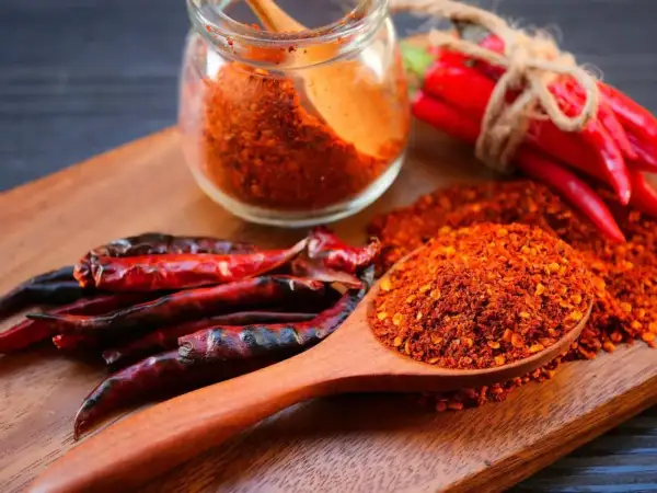 Ein Holzlöffel voller Cayennepfeffer-Flocken zeigt, woraus Cayennepfeffer hergestellt wird: getrocknete Chilischoten.