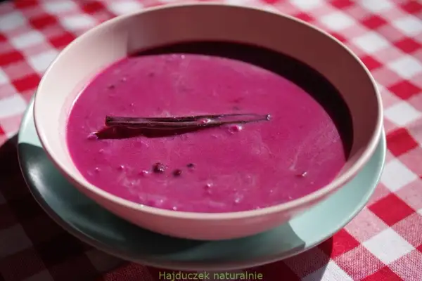 Aksamitna zupa jagodowa z laską wanilii, podana w miseczce na kraciastym obrusie.