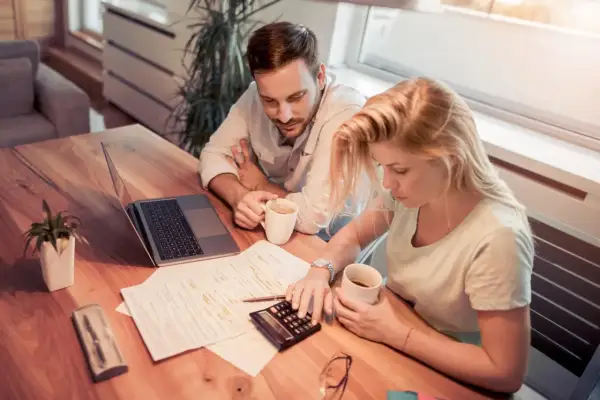 Couple calculant la refacturation de la taxe foncière pour un bail commercial, avec un ordinateur portable et des documents sur la table.