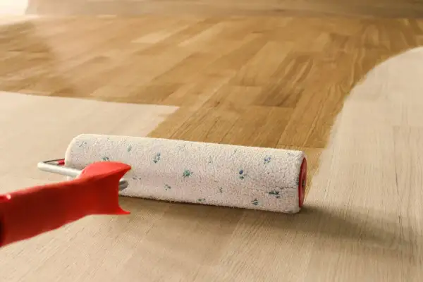 Rullo per verniciatura parquet in azione, che stende una mano di vernice su un pavimento in legno chiaro, creando un effetto bagnato e lucido.