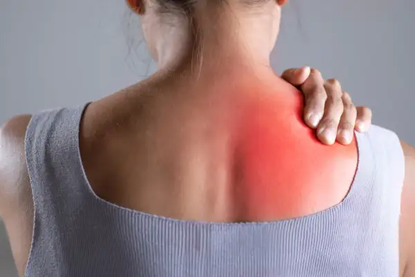 Donna con mano sulla spalla, evidenziata un'area rossa che indica dolore in mezzo alle scapole.