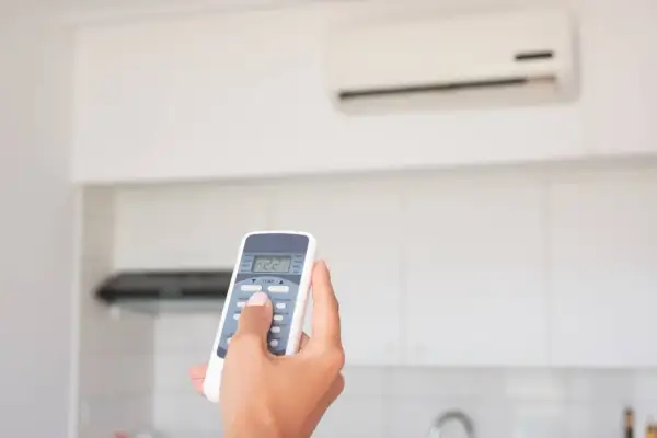 Mano che regola il telecomando del condizionatore in modalità "DRY" per un clima più asciutto.