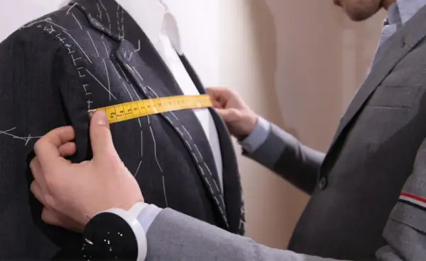 Sarto misura la giacca con metro giallo, prendendo nota della lunghezza braccio uomo per una vestibilità perfetta.