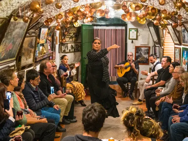 Artistas flamencos de Granada actúan en un tablao íntimo, con una bailaora en primer plano y un guitarrista acompañando.