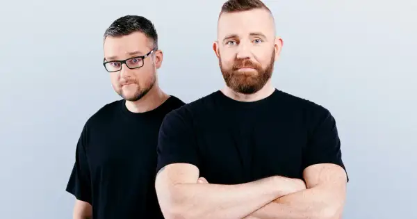 Dwóch mężczyzn w czarnych koszulkach, jeden w okularach, drugi ze skrzyżowanymi rękami. Wyglądają jak duet Catz n Dogz.