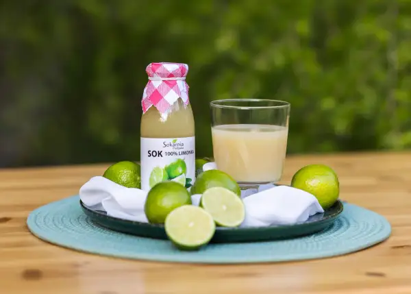 Butelka soku z limonki i szklanka orzeźwiającego napoju, otoczone świeżymi owocami. Odkryj sok z limonki właściwości!