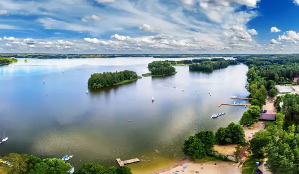 Malownicze zalewy w Polsce z żaglówkami, wyspami i plażą pełną wypoczywających ludzi.