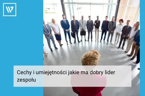 Grupa ludzi w garniturach stoi w kręgu, słuchając swojego **team leadera**.