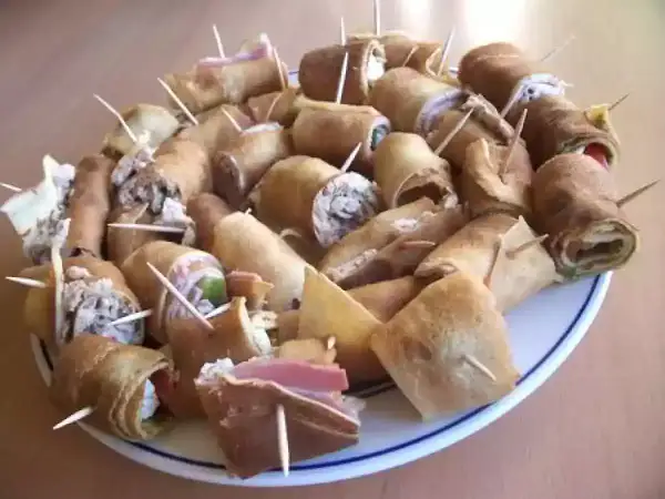 Assiette de crêpes roulées garnies, parfaites pour un apéro convivial. Des bouchées savoureuses prêtes à être dégustées.