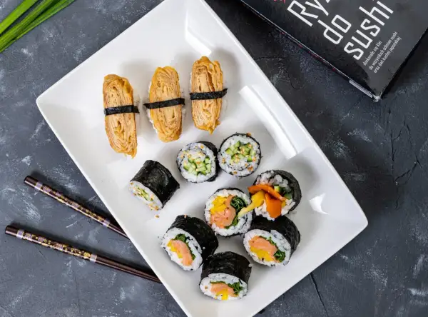 Pyszne domowe sushi przepis na talerzu: nigiri z omletem tamago, rolki z łososiem i warzywami, ogórkiem i sezamem.