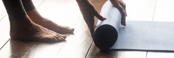 Pieds nus sur un parquet, une main déroule un tapis bleu pour une séance de sport à la maison.