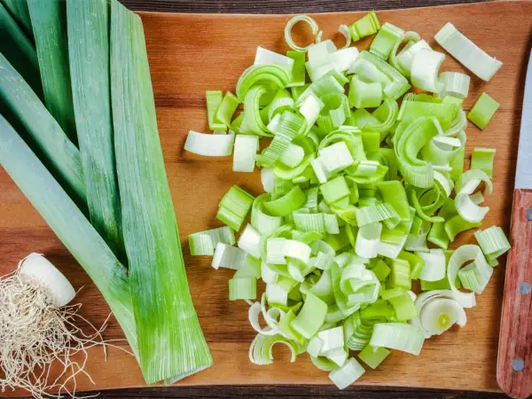 Frischer Lauch, bereit für leckere porree rezepte. Ganze Stangen und fein geschnittene Ringe liegen auf einem Holzbrett.