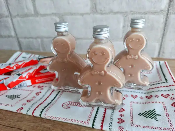 Trzy buteleczki likieru w kształcie ludzików z piernika, obok batoniki Kinder.