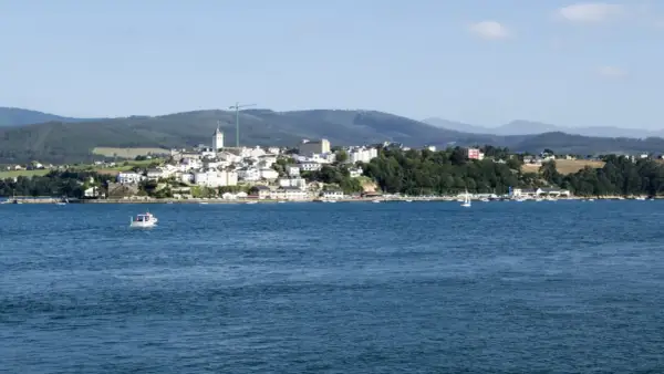 Vista del mirador de Ribadeo con casas blancas y el mar azul. Un pequeño barco navega en la distancia.