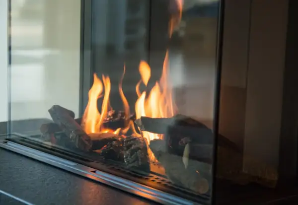 Flammen tanzen um Holzscheite in einem modernen Kamin. Ein Blick, der zeigt, wie man Ascheflecken entfernen kann, ohne die Gemütlichkeit zu stören.