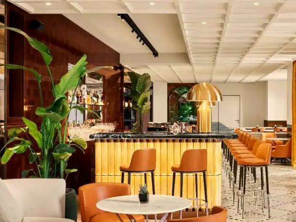 Interni eleganti del Bulgari Hotel Roma: bancone bar dorato, sedie in pelle arancione, piante lussureggianti e un'atmosfera sofisticata.