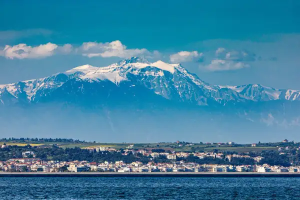 Majestatyczny góra Olimp, pokryta śniegiem, góruje nad nadmorskim miasteczkiem.