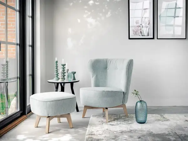 En bekväm fåtölj i turkos nyans, med en matchande pall och en blå vas med blommor.