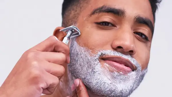 Uomo con schiuma da barba aggrappante prima della rasatura, mentre usa un rasoio di sicurezza.