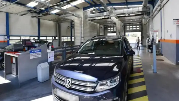 Un coche oscuro en un centro de inspección técnica, listo para pasar la ITV. El personal revisa los papeles.
