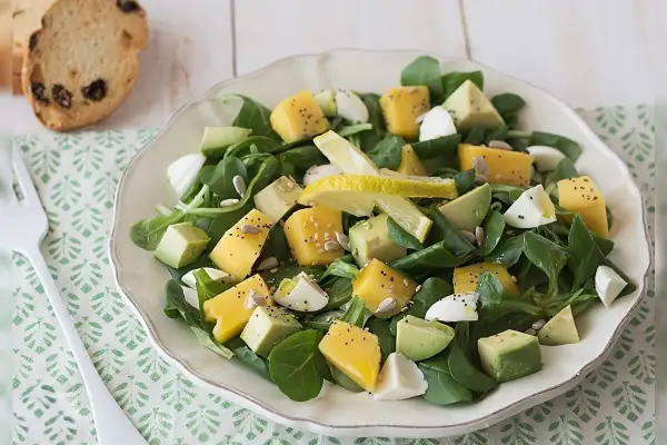 Deliciosa ensalada de lechuga con cubos de queso amarillo, aguacate, huevo cocido y semillas.